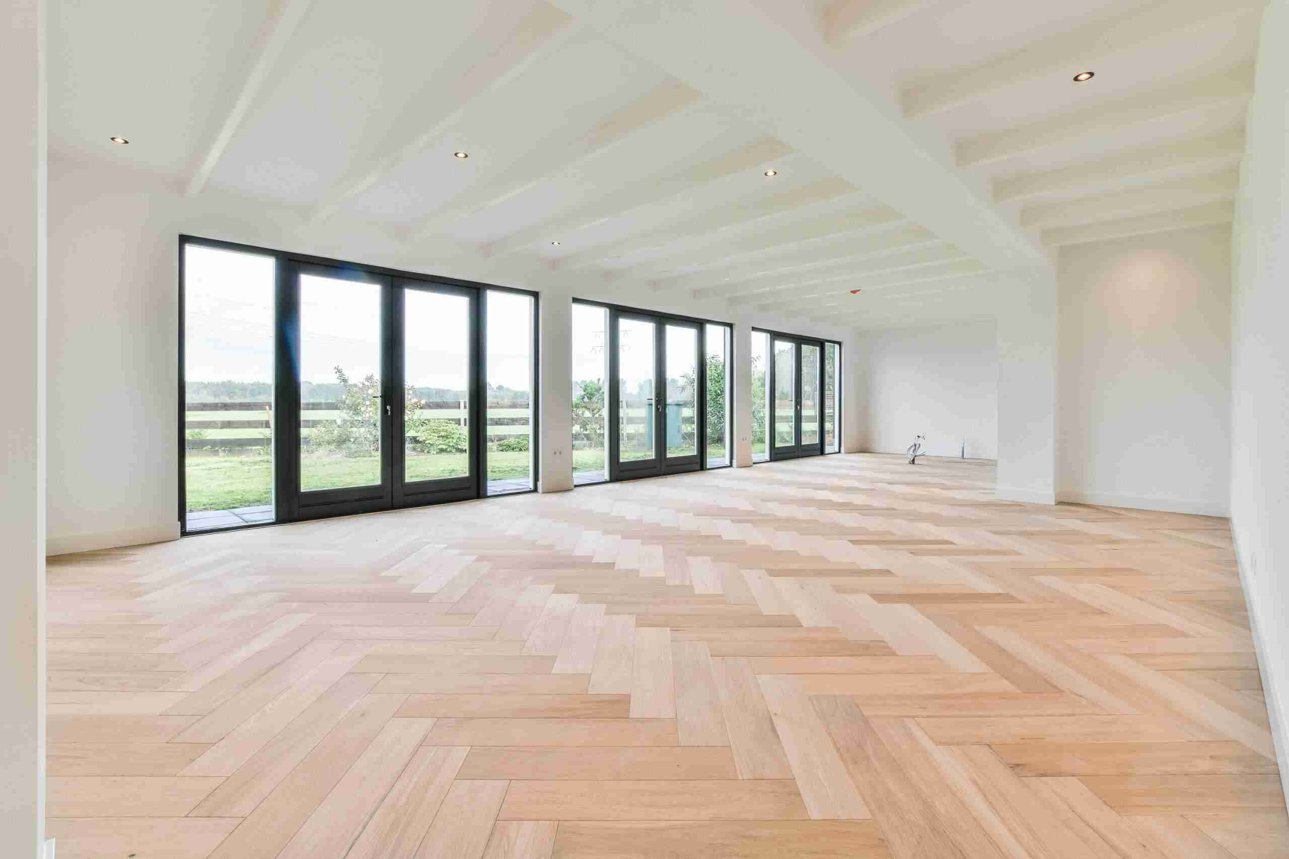 Wide view of a living space featuring freshly refinished hardwood floors and white baseboards.